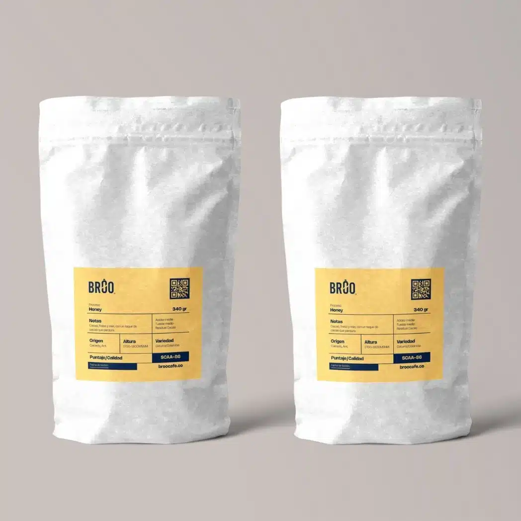 Café de especialidad Broo en dos bolsas blancas, proceso miel, Caicedo Antioquia, etiquetas amarillas y QR.