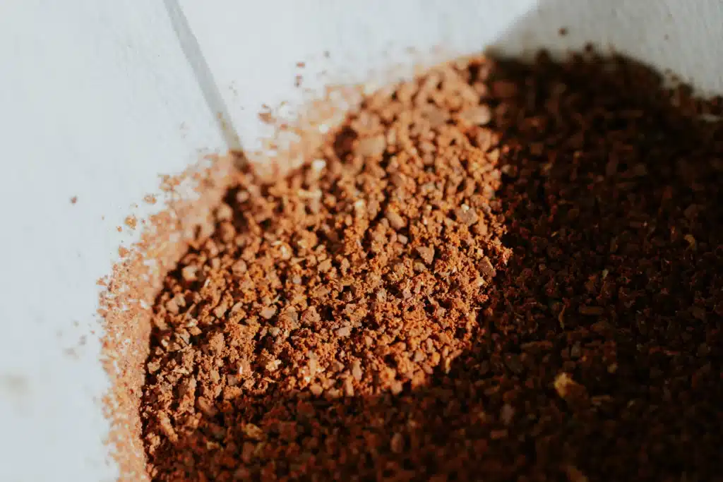 Montón de café recién molido de color marrón sobre una superficie blanca, con partículas de distintos tamaños