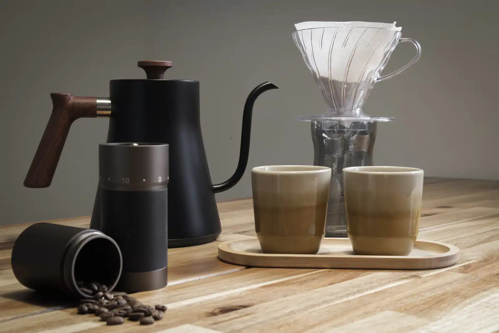 Hervidor de cuello de cisne, molino manual, V60 y dos tazas sobre una mesa de madera para preparar café en casa