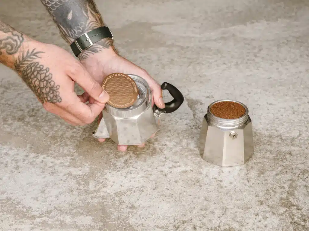 Cafetera italiana moka abierta con el filtro lleno de café molido, lista para cerrar y llevar al fuego