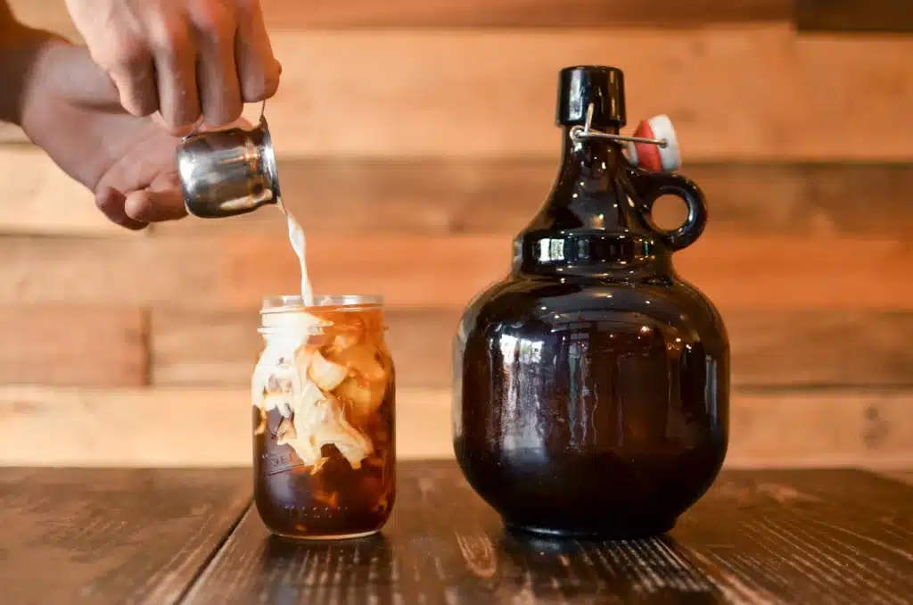 Leche servida sobre un frasco de vidrio con cold brew y hielo, junto a una botella ámbar de concentrado