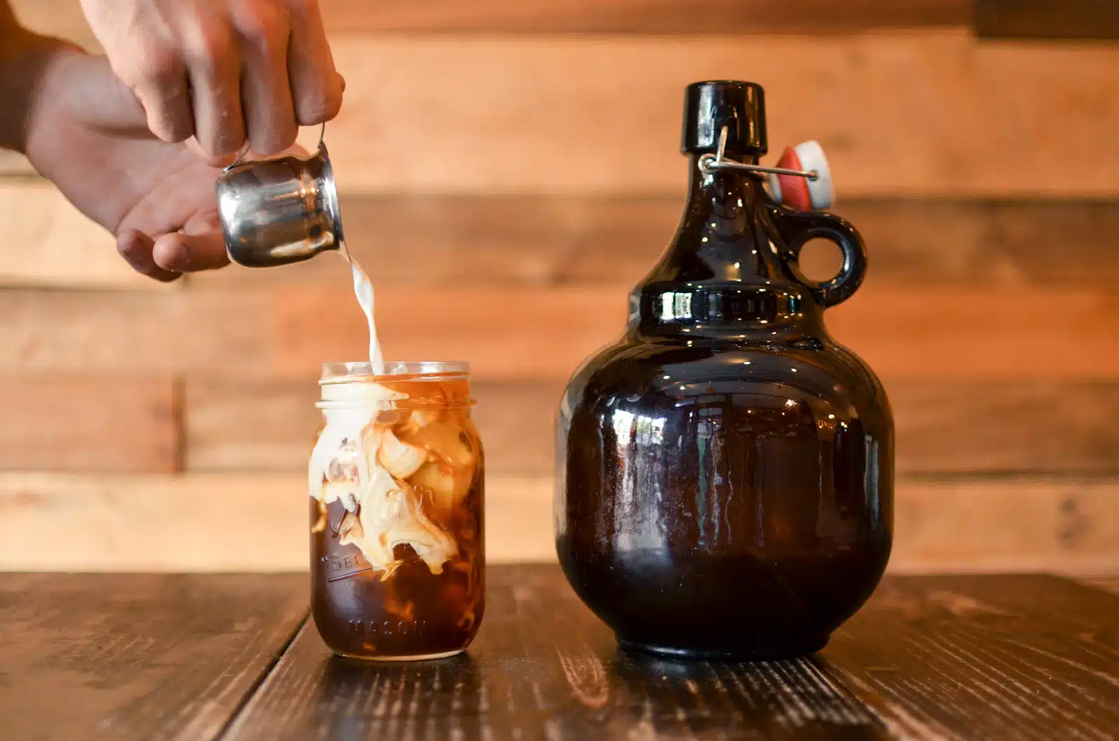 Leche servida sobre un frasco de vidrio con cold brew y hielo, junto a una botella ámbar de concentrado