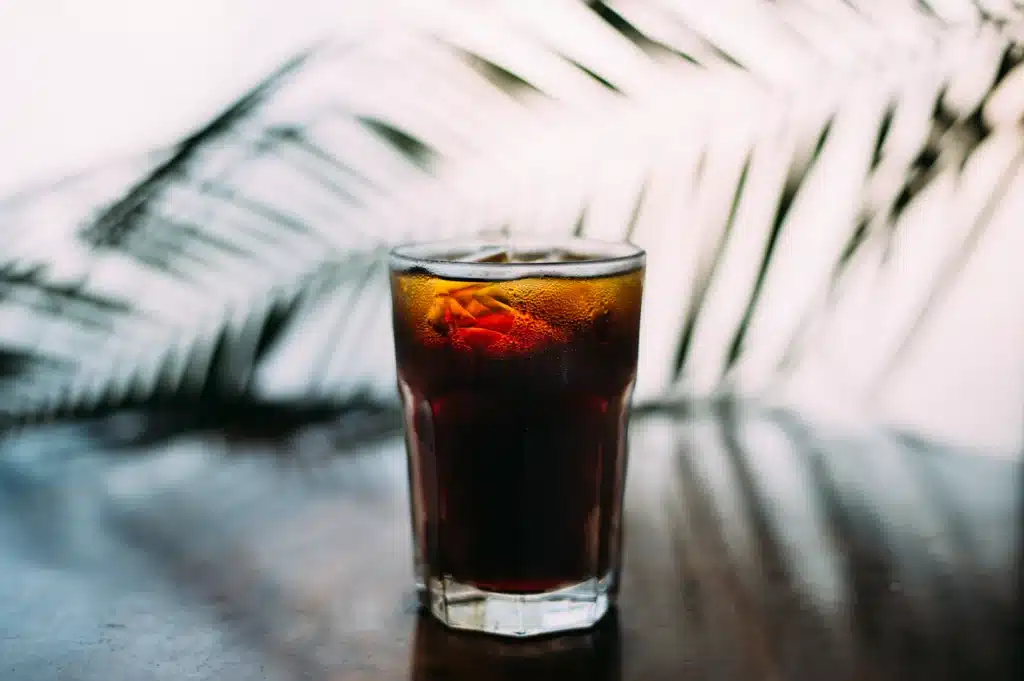 Vaso de cold brew oscuro con hielo sobre una mesa, iluminado por luz natural y sombras de hojas