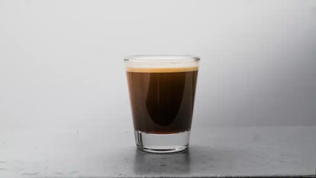 Shot de espresso con crema en un vaso de vidrio pequeño sobre una superficie gris