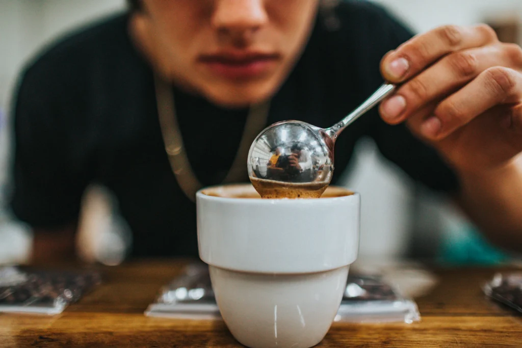 Catador probando café con una cuchara de catación sobre una taza blanca durante una evaluación de calidad