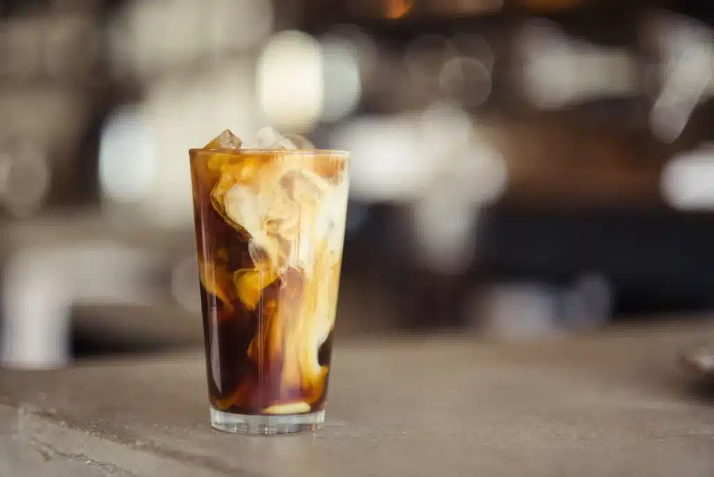 Vaso alto de café frío con hielo y leche mezclándose en remolinos sobre una barra