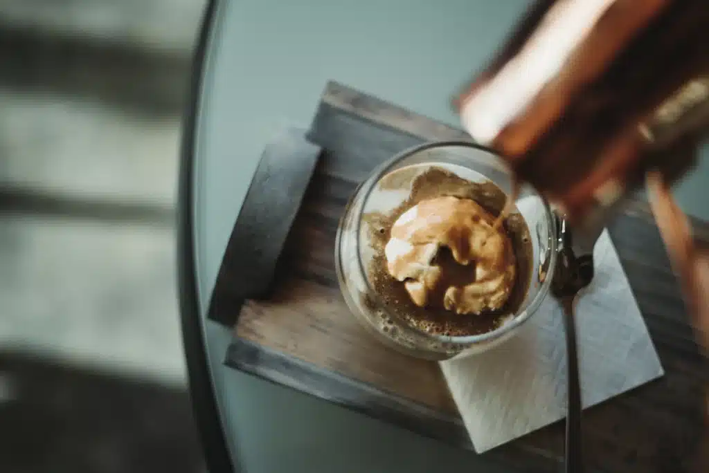 Café recién preparado vertido sobre helado de vainilla en un vaso de vidrio, preparación de un affogato