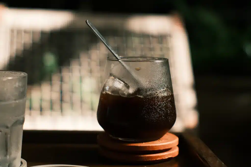 Vaso de iced coffee con hielo y una cuchara larga sobre posavasos, junto a un vaso de agua