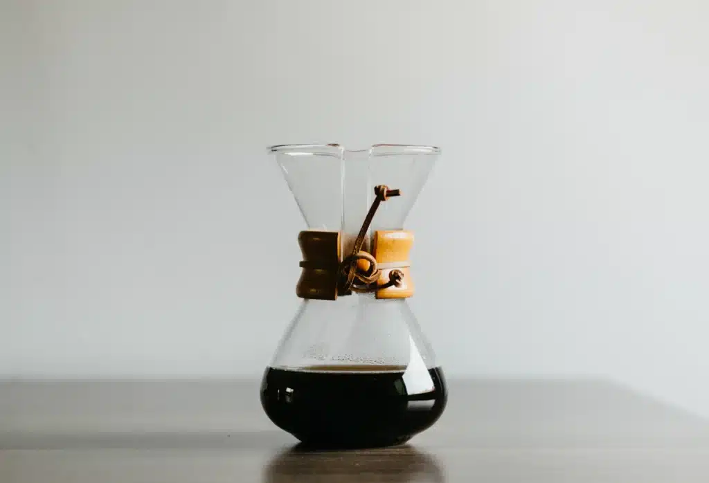 Cafetera Chemex de vidrio con cuello de madera y café recién preparado sobre una mesa