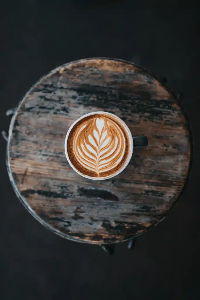 Capuchino en una taza blanca con espuma de leche y dibujo de arte latte, visto de cerca sobre una mesa