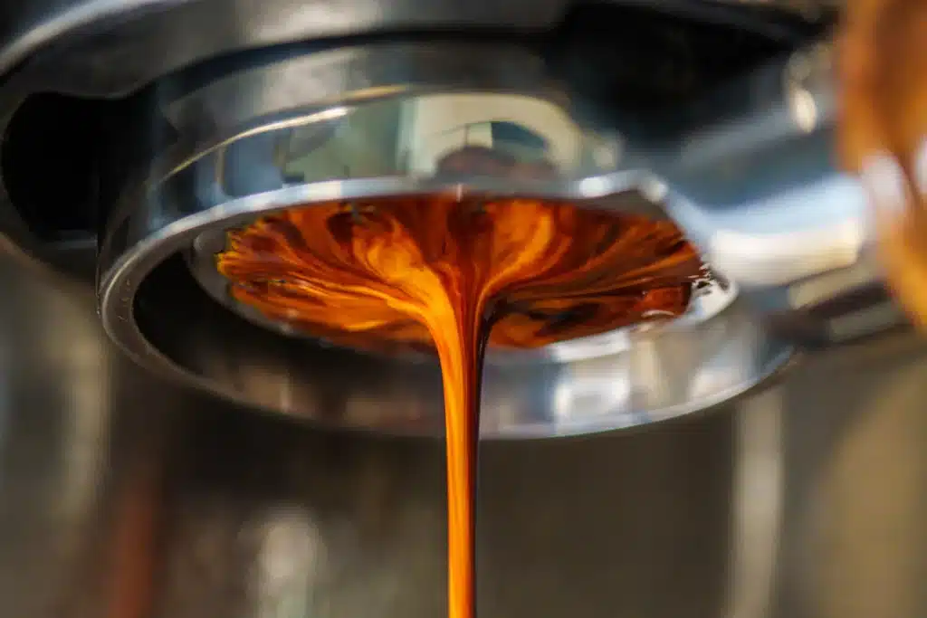 Espresso recién extraído cayendo del portafiltro de una máquina de café a una taza