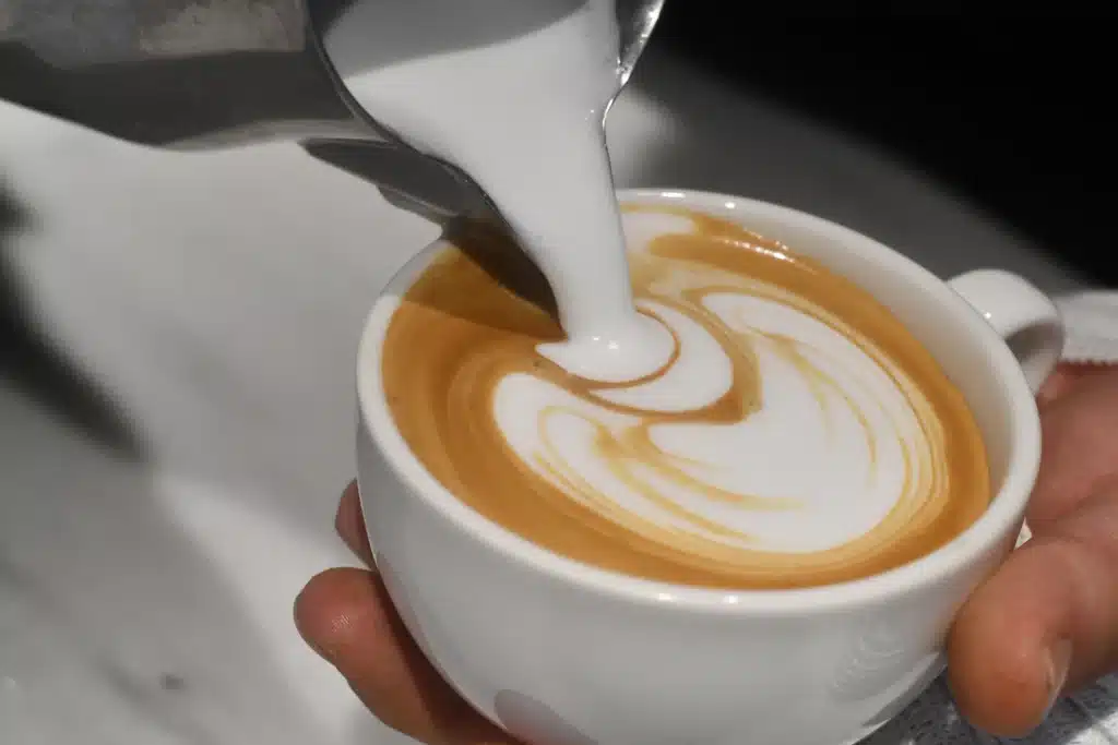 Persona sirviendo leche espumada desde una jarra en una taza de café