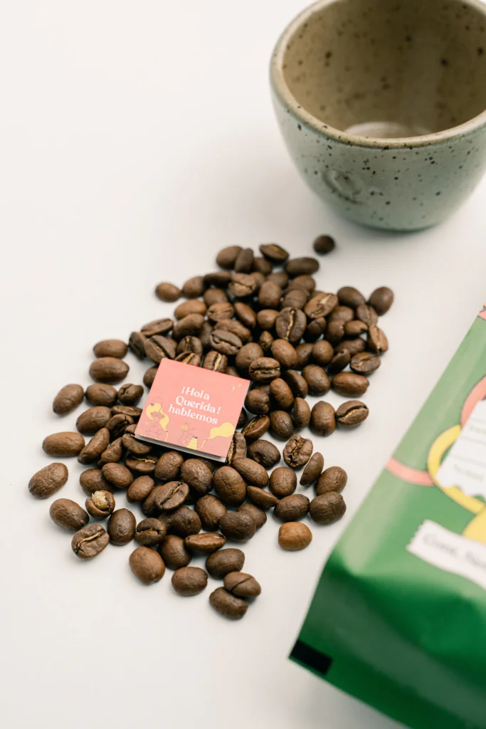 Granos de café junto a una tarjeta pequeña y una taza